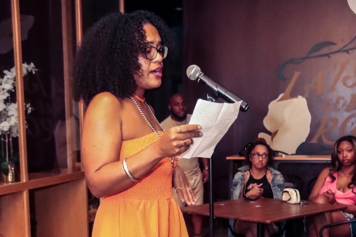 A poet in an orange dress performing on stage