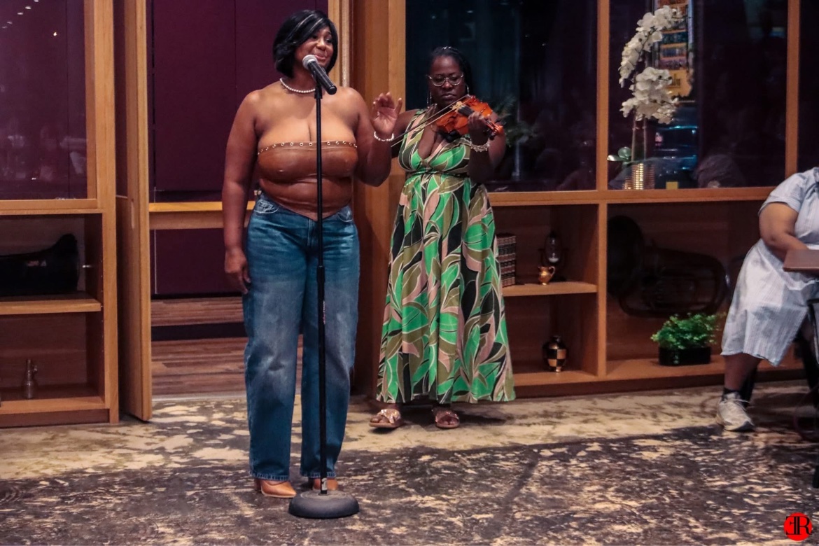 Woman singing at a microphone with a violinist performing beside her