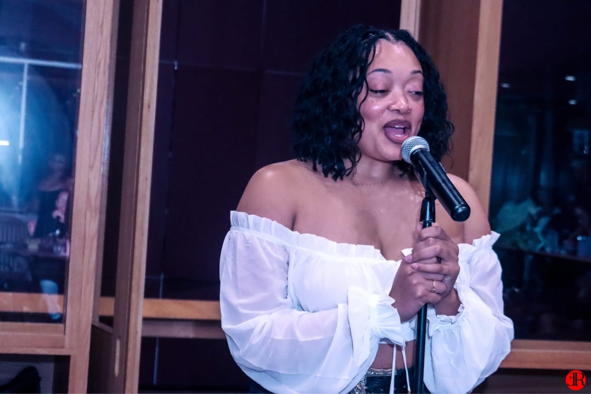 Woman in a white top singing into a microphone on stage